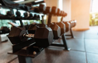 Spor salonunda günbatımının ışığı altında sıra sıra halterler.