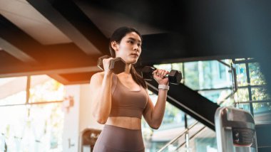 Genç, güzel, zayıf bir kadın spor salonunda halterle egzersiz yapıyor.