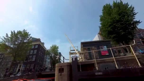 晴れた日に夏にアムステルダムの家に沿って運河沿いのボートに乗る — ストック動画
