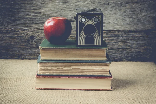 Books and vintage camera with apple on rustic background with re — Stock Photo, Image