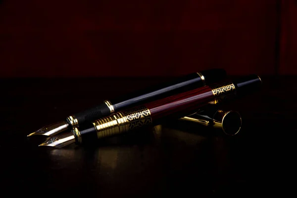 Fountain pens, beautiful fountain pens in detail on black surface, low key image, selective focus.