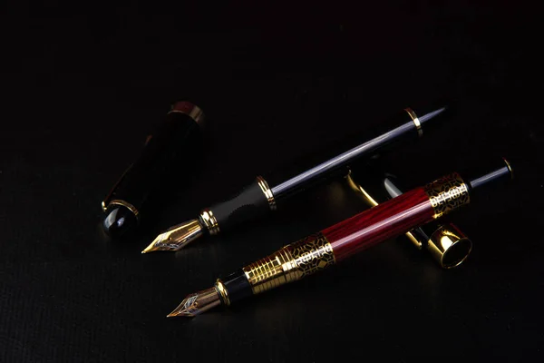 Fountain pens, beautiful fountain pens in detail on black surface, low key image, selective focus.
