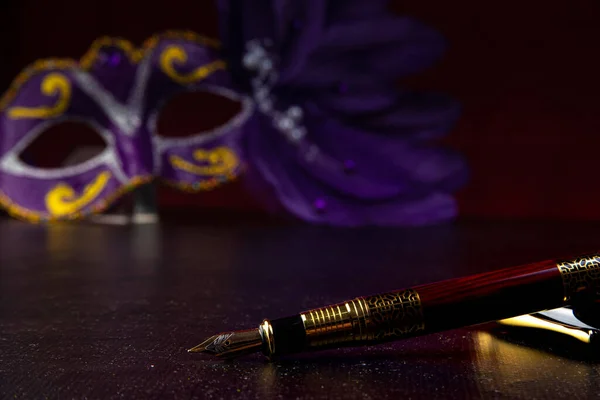 Fountain pens, beautiful fountain pens in detail on black surface with Venetian mask in the background, low key image, selective focus.