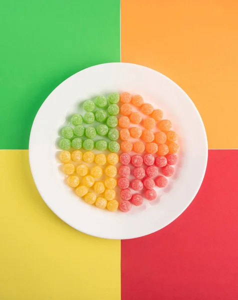 Gummy candy, arrangement of gummy candy arranged by color on a white plate on a colored surface.