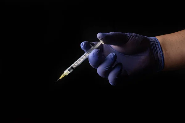 Covid 19 vaccine, immunity and medical treatment. Hand wearing glove holding a syringe and needle. black background, selective focus.