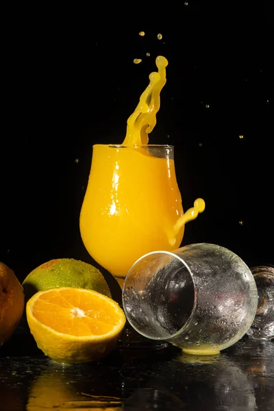 Orange juice, splash in beautiful glasses of orange juice and oranges around, black background, selective focus.