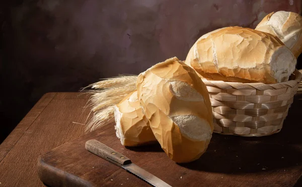 Breads, beautiful breads in a basket with wheat branch on wooden surface, dark abstract background, selective focus.