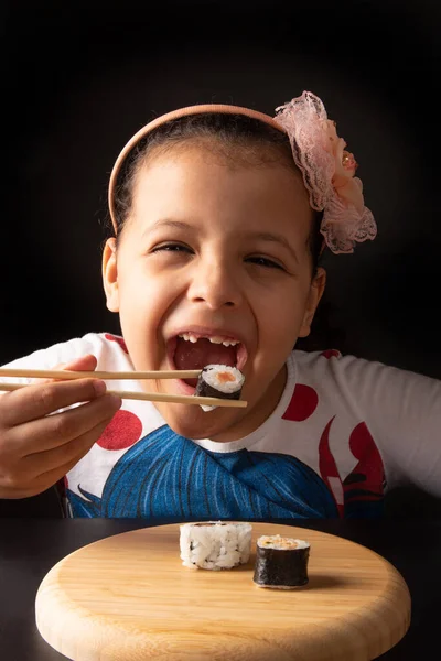 Sushi, beautiful girl eating sushi using chopsticks, black background, selective focus.