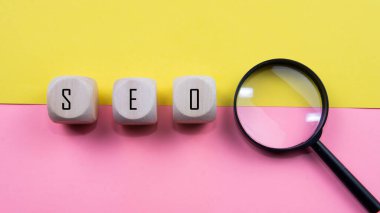 Arama motoru optimizasyon konsepti, ahşap zarlarda SEO kısaltması trafiği web sitesine yönlendirme fikri. Tahta zarlara, büyüteçlere ve izole edilmiş pembe ve sarı arkaplana odaklan..