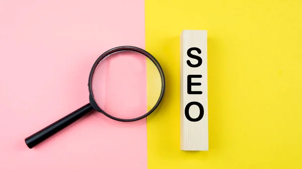 Search Engine Optimization ranking concept, abbreviation SEO on the wooden dice as an idea of promote traffic to website. Selective focus on wooden dice, magnifying glass and a mouse isolated pink and yellow background.