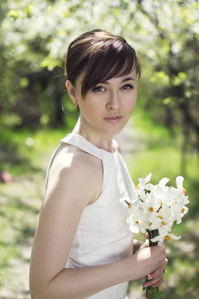 Young woman stay  in spring orchard trees, holding flower at her hand. Concept of the first date. the gentle image of the bride — Stock Photo, Image