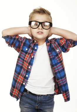 Funny child.fashionable little boy in glasses, jeans, white t-shirt and plaid shirt.stylish kid in sport shoes. fashion children closes his ears  hands
