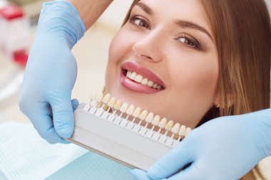 Avrupalı güzel bir kadın sağlıklı diş beyazlatıcı ile gülümsüyor. Diş bakımı konsepti. Farklı tonlarda implantlar.