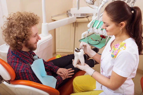 Portrait of female dentist show a sample of teeth with caries to his patient at office. Dental care Concept. Dental inspection is being given to  Beautiful man surrounded by dentist and his assistant — Stock Photo, Image