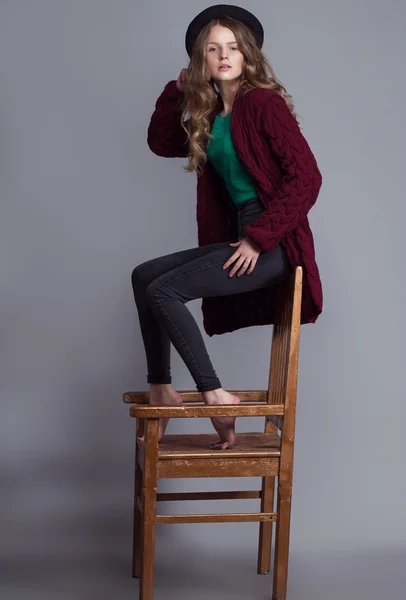 カジュアルウェア(ニットカーディガン、ジーンズ、緑のt-shir)で若い美しい女性モデルのファッションポートレート。ブーツなしで、帽子と自然なメイクアップは、椅子に座って彼女の顔に。スペースのコピー. — ストック写真