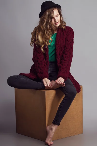 Moda Portret młodej pięknej kobiety model w casual Wear (dzianinowy sweter, dżinsy i zielony t-Shir). bez butów, w kapeluszu i naturalny makijaż na jej twarzy siedzi na drewnianej kostki. Kopiuj przestrzeń. — Zdjęcie stockowe