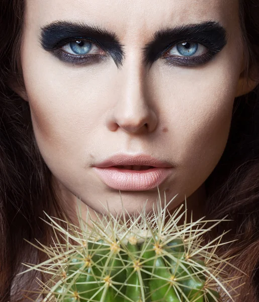 Sexy Beauty Girl with natural Lips and arty black make up on her eyes. Provocative Make up. Luxury Woman with Blue Eyes. Fashion Brunette Portrait on grey background holding a green cactus. Gorgeous Woman Face. Long Hair — Stock Photo, Image