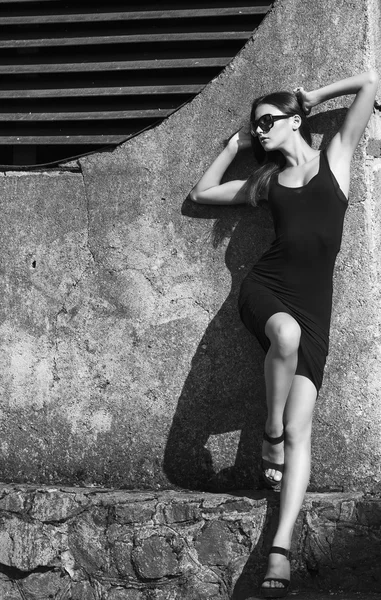Mode portret van jonge mooie brunette meisje in sexy zwarte jurk en zonnebril. Buiten schot. Stedelijke stijl — Stockfoto