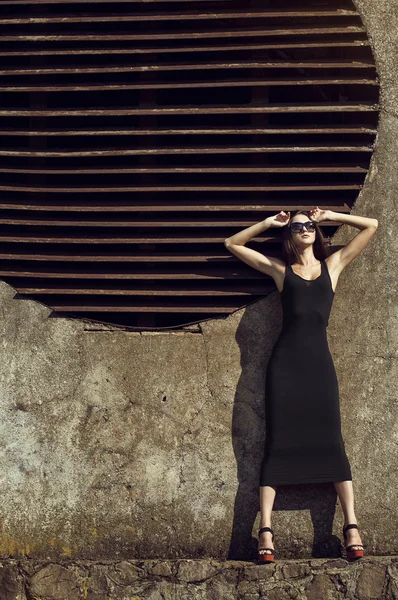 Retrato de moda de joven chica morena hermosa en vestido negro sexy y gafas de sol. Un disparo al aire libre. Estilo urbano —  Fotos de Stock