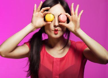 Güzel genç kadın ile temiz taze cilt, mükemmel makyaj ve çivi ile pasta / arka plan Macaroons elleri üzerinde parlak pembe. Moda fotoğraf.