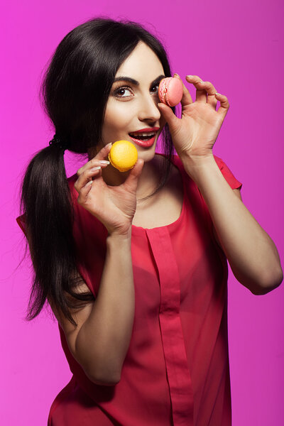 Beautiful Young Woman with Clean Fresh Skin, perfect make up and nails with cake / Macaroons in her hands over bright pink background. Fashion photo.