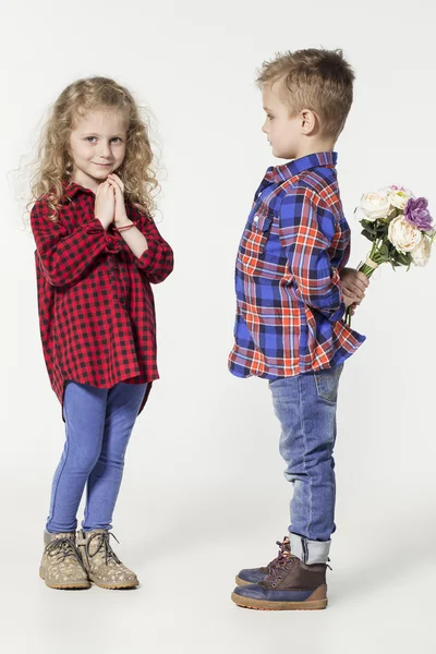 Bambini simpatici e adorabili. bambino e ragazza alla moda in jeans e camicie a quadri. Il bambino dà fiori alla ragazza. bambini alla moda in scarpe casual. moda bambini — Foto Stock