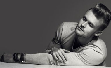 Advertising wrist watch concept. Beautiful (handsome) muscular male model with perfect body in grey jumper and with the clock on his hand. Street style. Black and white, monochrome studio shot