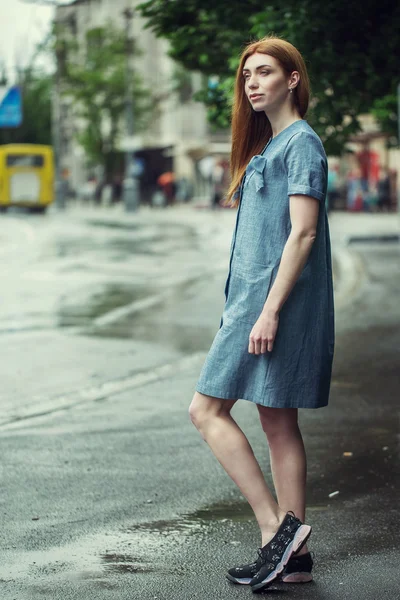 Beautiful stylish young girl dressed in casual clothes (dress and sneakers) walks through the streets of the city after the rain. the concept of fashion wear for women — Stock Photo, Image