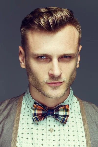 Emotive portrait of handsome young man in retro shirt, scottish in cell bow-tie and round unusual sunglasses posing over gray background. White shiny smile and healthy skin. Urban style. Studio shot — Stock Photo, Image
