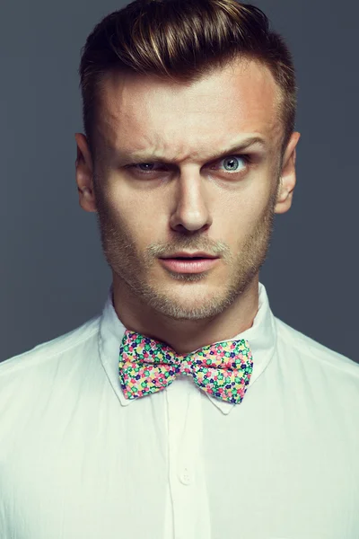 Emotive portrait of smiling/serious/shocked handsome young man in white shirt and color bow-tie posing over gray background. White shiny smile and healthy skin. Urban style. Studio shot — Stock Photo, Image