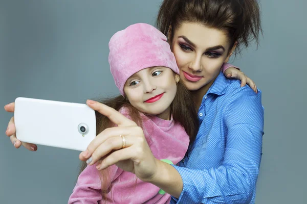 Dos hermosas hermanas (chicas) haciendo selfies en el estudio. Copiar espacio. Piel y maquillaje perfectos. Ropa casual —  Fotos de Stock