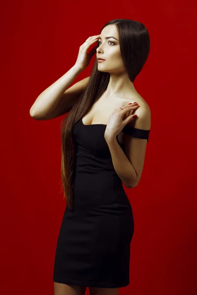 美しいセクシーな女性の肖像画、完璧なメイク、髪型、爪。美しいブルネットの女の子。リトル ブラック ドレスのコンセプトです。赤の背景に撮影スタジオ — ストック写真