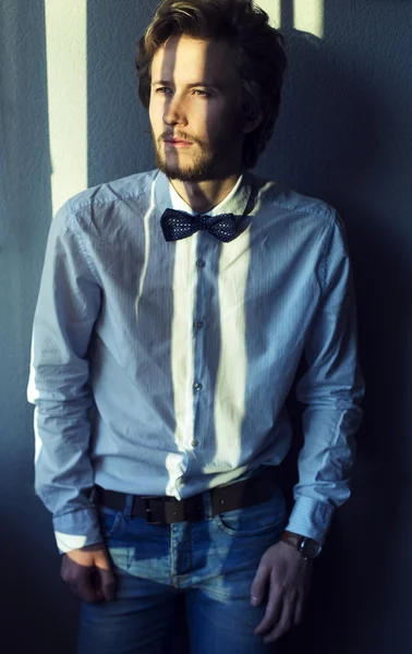 Emotive portrait of handsome young man in white shirt andblack bow-tie posing over gray background.  Urban style. Studio shot