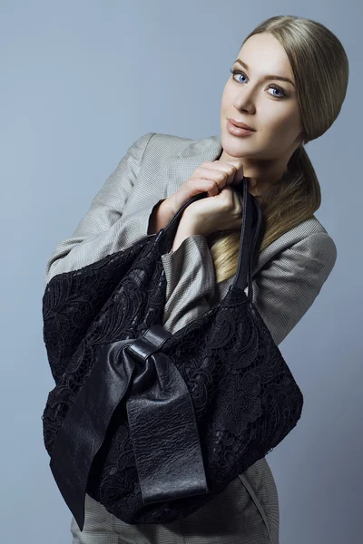 Mujer sexy rubia joven en un traje de negocios y con bolsa de rejilla negra sobre un fondo gris. Captura de estudio — Foto de Stock
