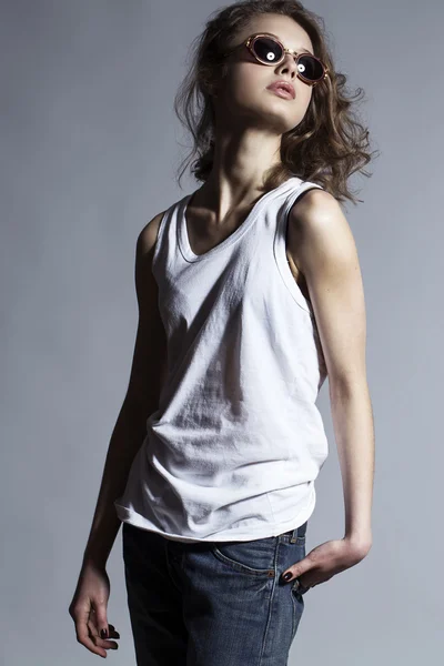 High fashion look. Portrait of a fashionable model with natural  make up and perfect skin, dressed in men's jeans, white shirt and stylish round glasses.  Studio shot