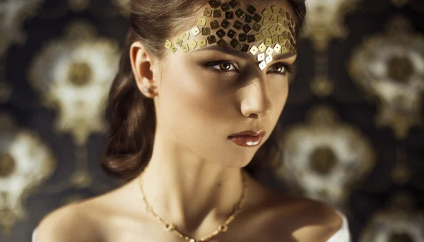 Fashion photo of brunette beauty with perfect make-up, skin and  body. Concept of gorgeous woman in golds square sparkles on her face, gold accessories posing on the vintage style background — Stock Photo, Image