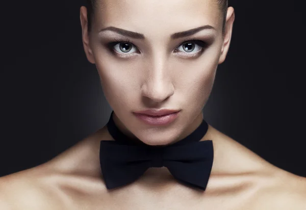 Portrait rapproché d'une dame sérieuse avec un maquillage des yeux fumé, les épaules nues et attacher un papillon sur son cou. Une peau parfaite. Prise de vue. Fond noir — Photo