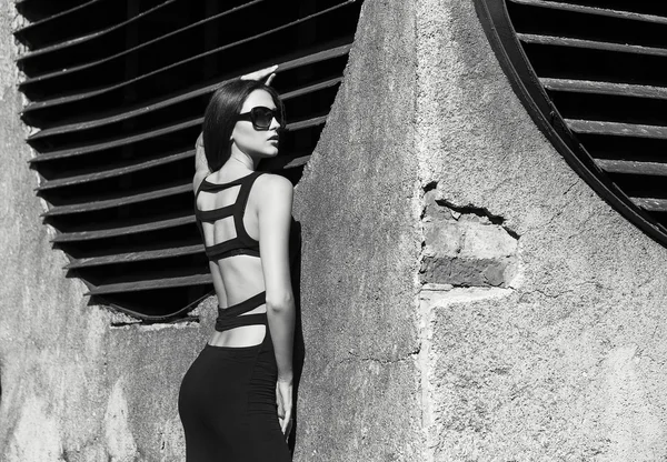 Fashion portrait of young beautiful brunette girl in sexy black  dresss and sunglasses. Vogue style. Outdoor shot. Black and white photo. Urban style — Stock Photo, Image