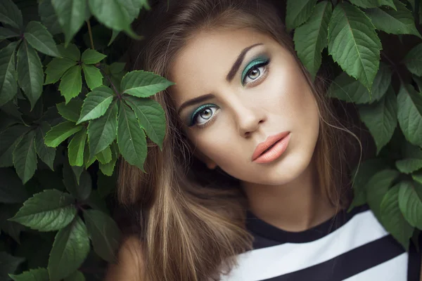 Sexy Beauty Girl with coral Lips. Provocative green Make up. Luxury Woman with Green Eyes. Fashion Brunette Portrait in wild leaves (grapes),  natural background. Gorgeous Woman Face. Long Hair