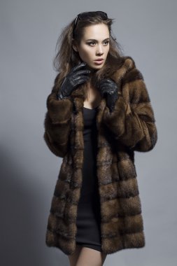 Sexy Beauty Girl with natural  Make up.  Fashion Brunette  Portrait of a girl dressed in fur coat,  black dress and sunglasses posing on a grey background. Retro style