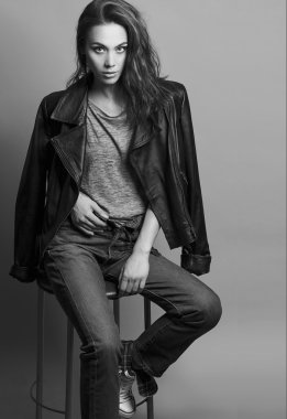 Portrait of a fashionable model with natural make up and perfect skin, dressed in men's jeans, grey shirt, black jacket and sneakers.  Studio shot. High fashion look. Monochrome (black and white)  photo