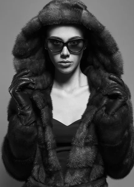 Sexy Beauty Girl with natural  Make up.  Fashion Brunette  Portrait of a girl dressed in fur coat,  black dress and sunglasses posing on a grey background. Retro style. Monochrome (black and white)  photo — Stockfoto