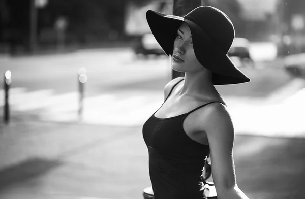 Fashion style portrait of young trendy girl walking along the street at sunset. Concept of a little black dress. perfect body and silhouette. a little black dress. perfect body and silhouette. — Stockfoto