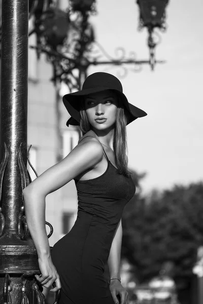 Fashion style portrait of young trendy girl walking along the street at sunset. Concept of a little black dress. perfect body and silhouette. Vintage style photo with custom white balance and some fine film noise added to the image — Stock Photo, Image