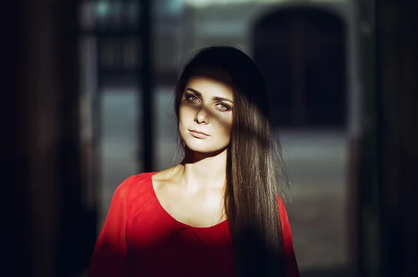 Fashion style portrait of young trendy girl walking along the street at sunset. Concept of a red dress. perfect body and silhouette. Vintage style photo with custom white balance, color filters, and some fine film noise added to the image — Stock Photo, Image