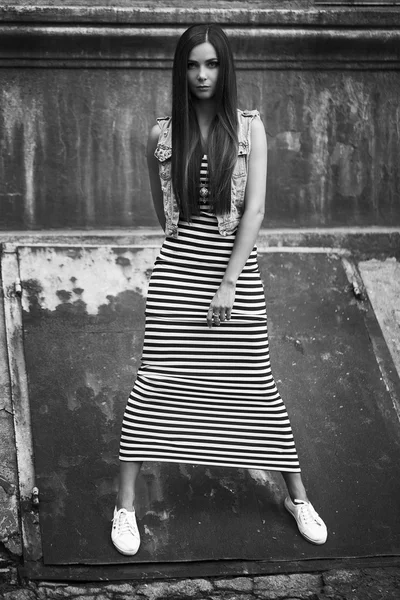 Fashion portrait of young beautiful brunette girl in trendy balck and white casual dress, white sneakers and jeans jacket posing alone over old wall. Vogue style. Outdoor shot — Stock Photo, Image