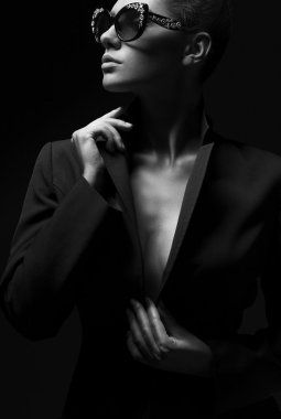 Portrait of a beautiful girl posing in studio in black jacket and fashion sunglasses. The concept of stylish and sexy women. perfect skin and body. Black and white photo