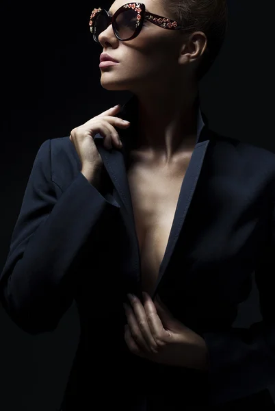 Retrato de una hermosa chica posando en estudio en chaqueta negra y gafas de sol de moda. El concepto de las mujeres elegantes y sexy. piel y cuerpo perfectos —  Fotos de Stock