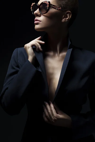 Portrait of a beautiful girl posing in studio in black jacket and fashion sunglasses. The concept of stylish and sexy women. perfect skin and body — Stock Fotó