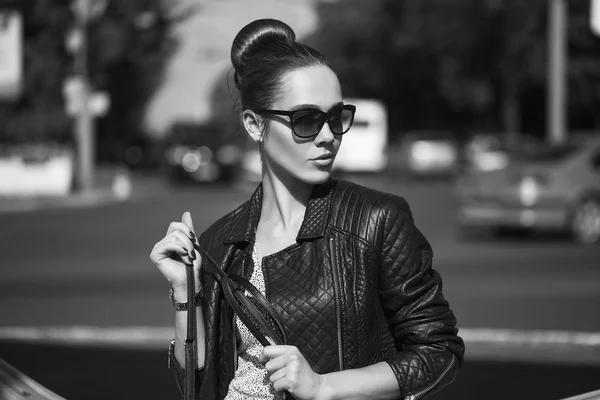 Concept de beauté féminine. Portrait de jeune fille à la mode en jean noir décontracté, veste noire, crop-top blanc, lunettes de soleil et petit sac posant dans la rue. Cheveux et peau parfaits. Style vogue. plan extérieur — Photo